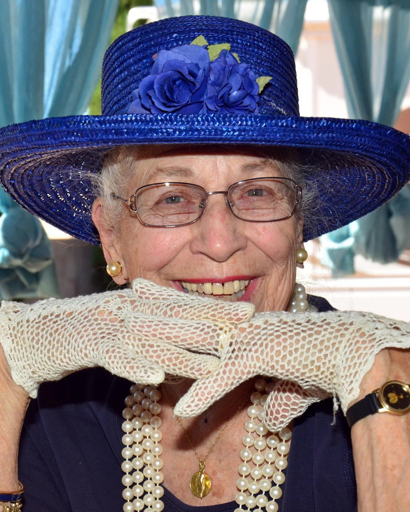 Elderly woman in blue hat, smiling.