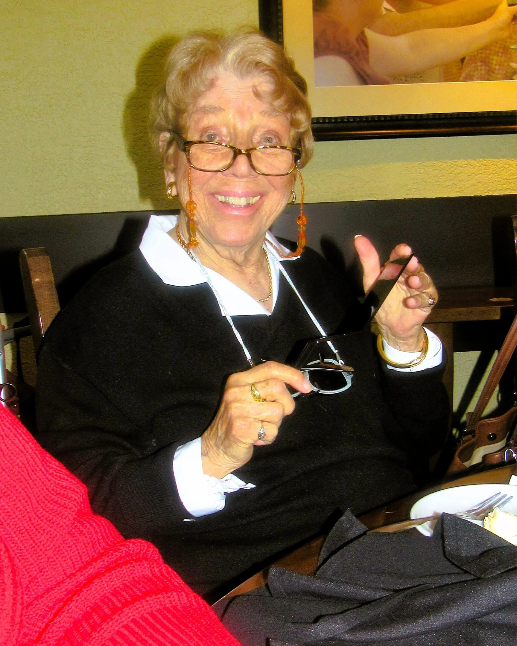 Elderly woman smiling and holding glasses.